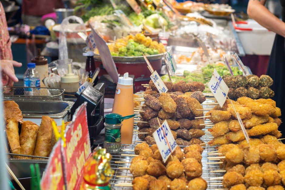 A vibrant street food stall offering a variety of skewers and snacks in a busy market sett