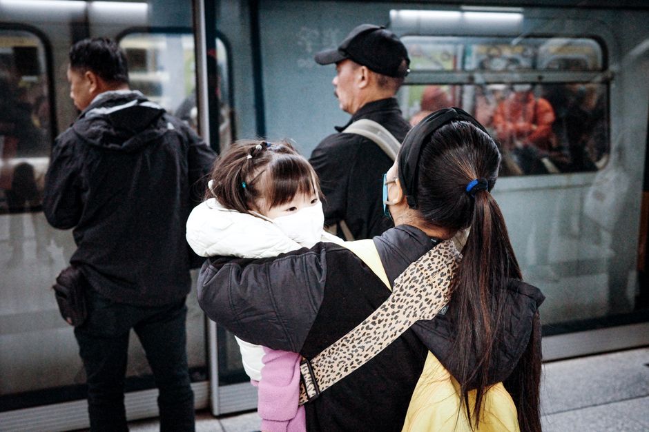 A woman and child wearing masks wait on a Kowloon railway platform. Urban commute scene.