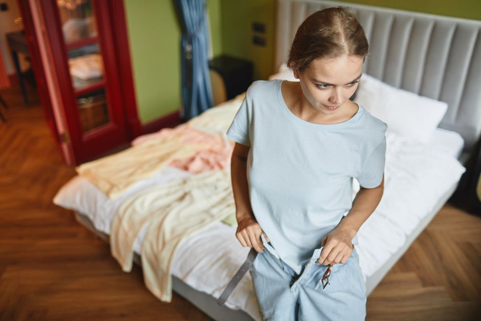 A young woman in a blue shirt dressing up in a modern bedroom, focusing on style and comfo