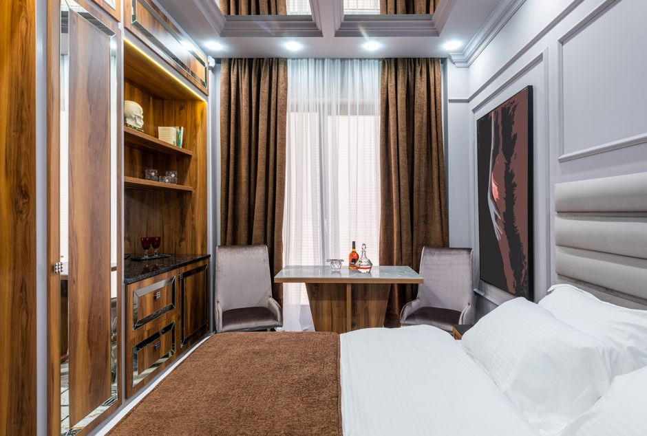 Bed with soft pillows and cover against table with bottle of alcoholic drink between armchairs in house