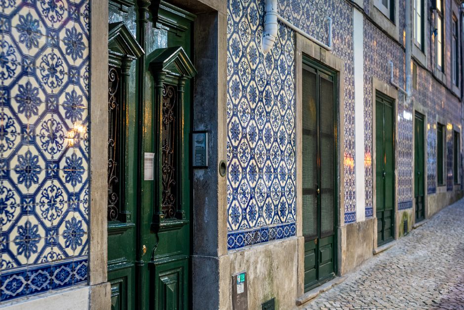 A picturesque street in Lisbon featuring iconic blue and white Portuguese tiles and green doorways.