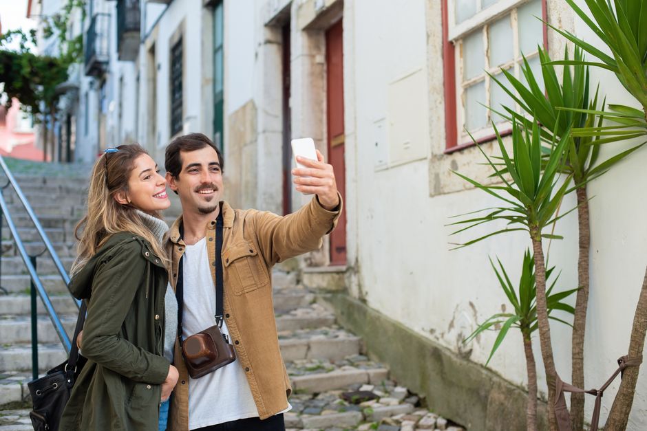 A happy couple taking a selfie in a picturesque alleyway during their travel adventure.