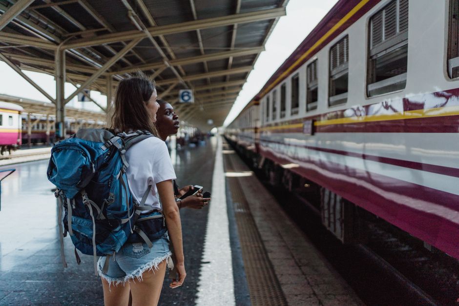 Two women with backpacks waiting at a train station platform for their next journey.