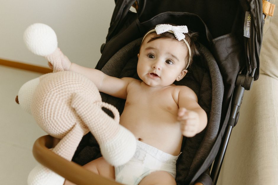 Cute baby girl in stroller holding a knitted toy. Happy childhood moment.