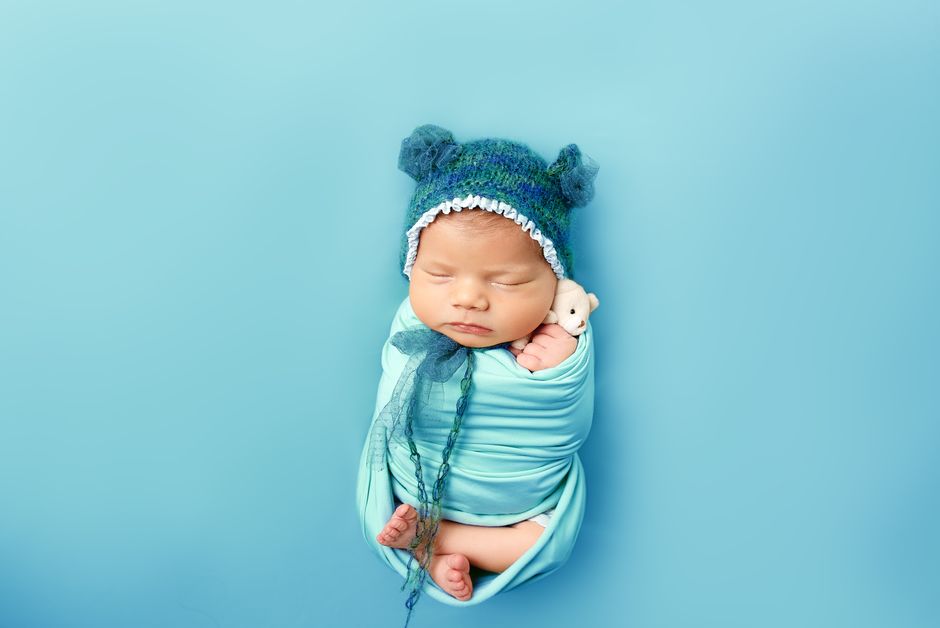 Adorable newborn baby wrapped in blue with a bear hat, peacefully sleeping.