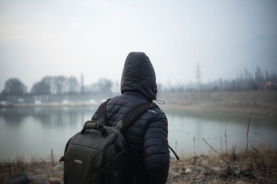 Person in a hoodie and backpack by a misty lake, capturing solitude