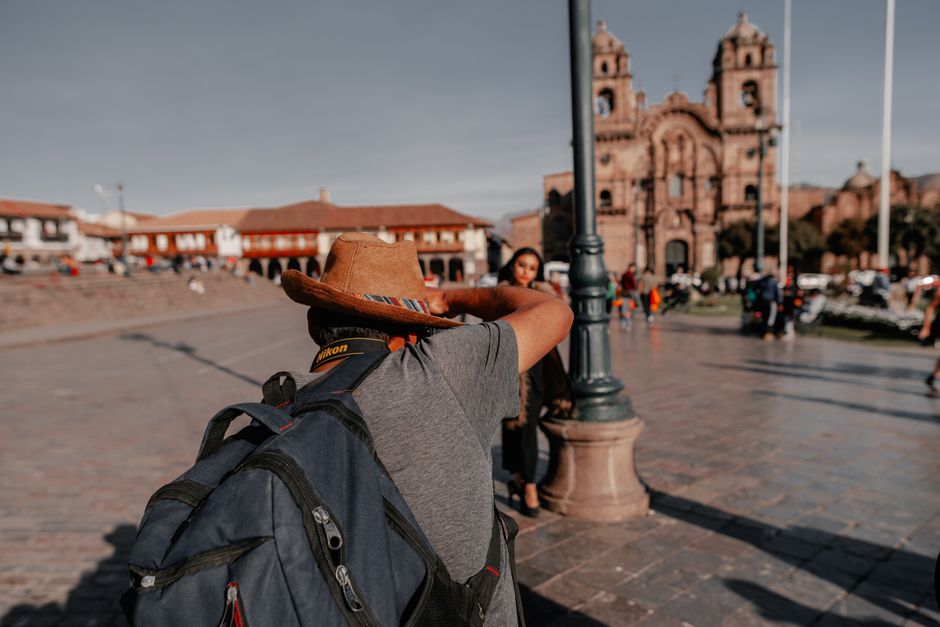 Adult backpacker photographing in a vibrant urban square with historic architecture.