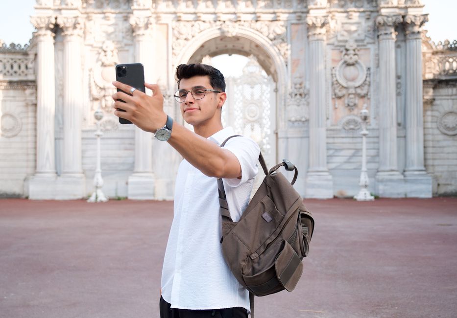 Young man capturing a selfie in front of Istanbul's Dolmabahçe Palace.