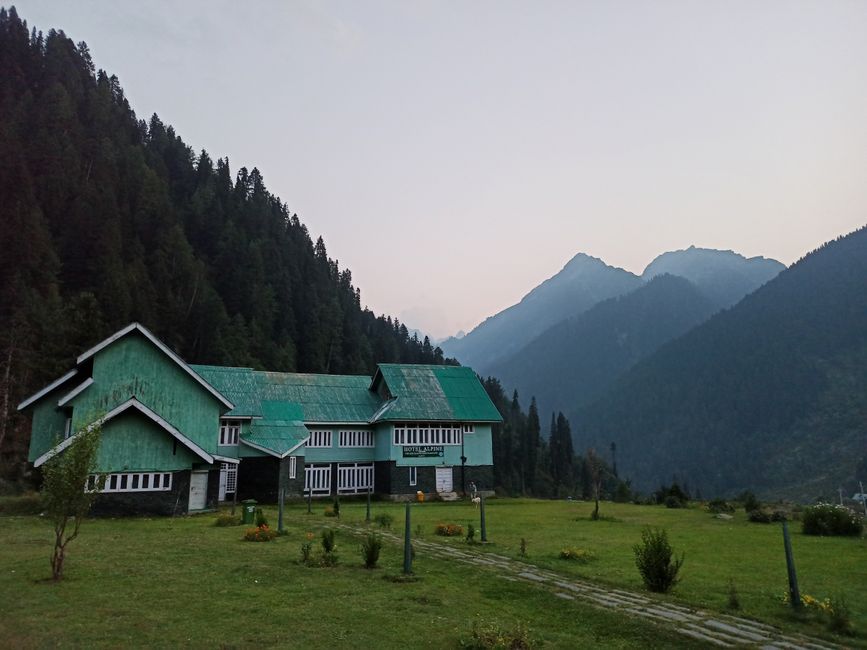 Scenic view of an alpine house amidst lush green valley in Pahalgam with mountainous backdrop.