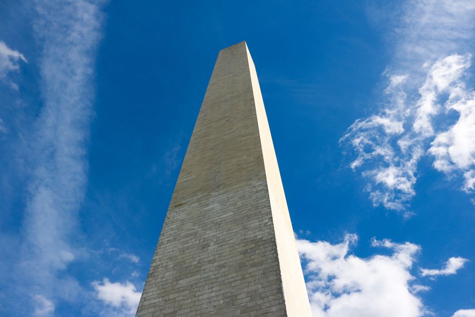 Low angle shot of the Washington Monument with a clear blue sky and clouds.