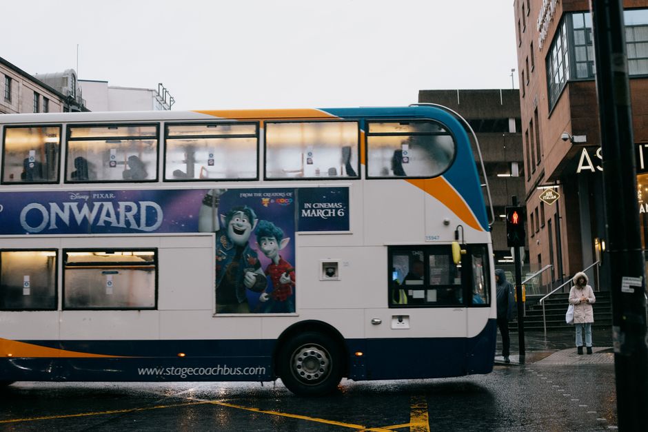Contemporary double decker bus with illustration driving on asphalt roadway near anonymous pedestrians and buildings in city