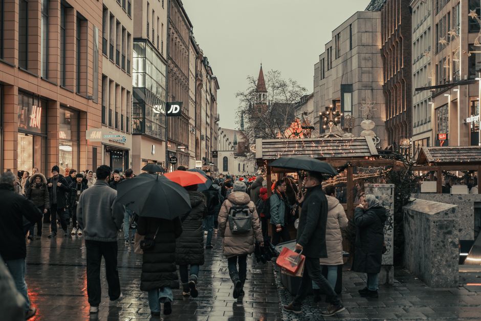 Bustling city street scene with people and holiday market on a rainy day.
