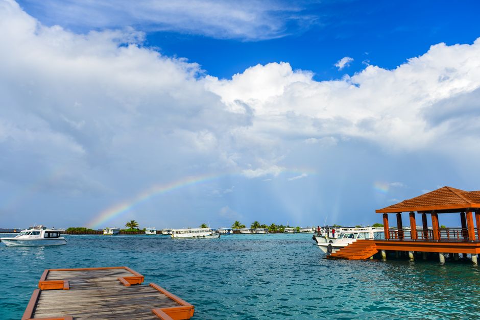 Scenic view of a tropical resort dock over clear waters with a rainbow in the sky.