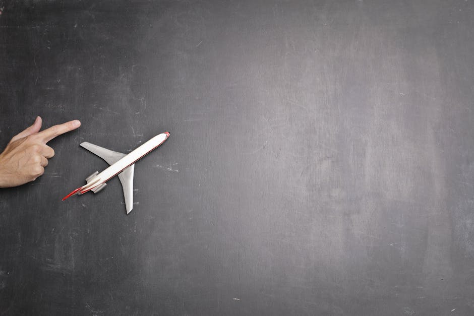 Top view of crop anonymous person indicating direction on blank blackboard with miniature airplane