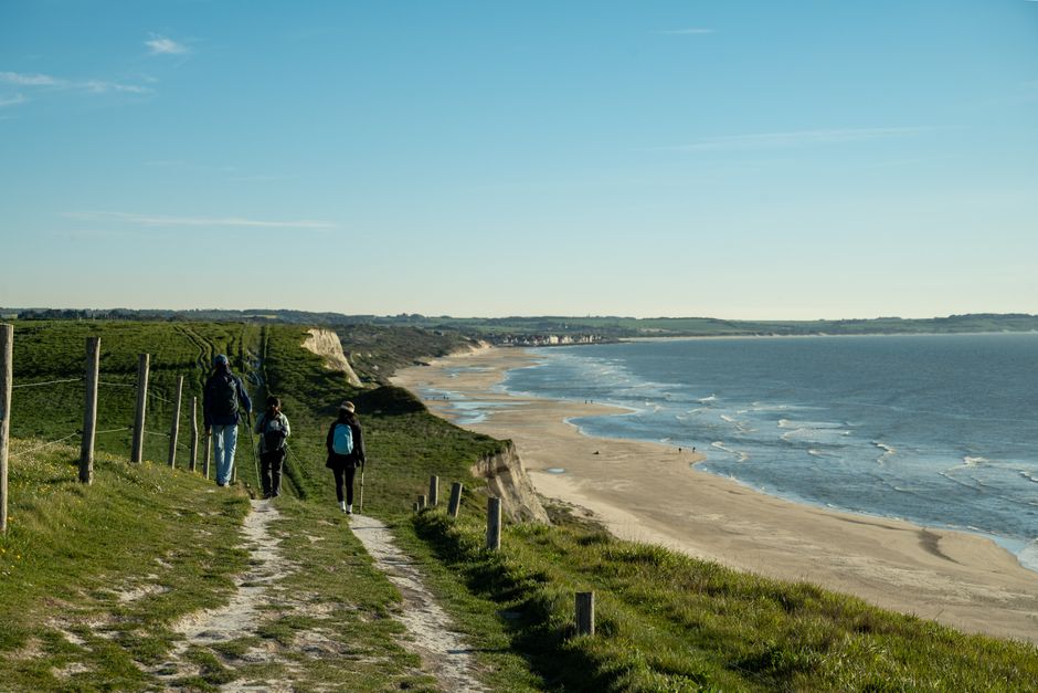 Three hikers enjoy a picturesque coastal path in Escalles, France, overlooking the sea and sandy beach.