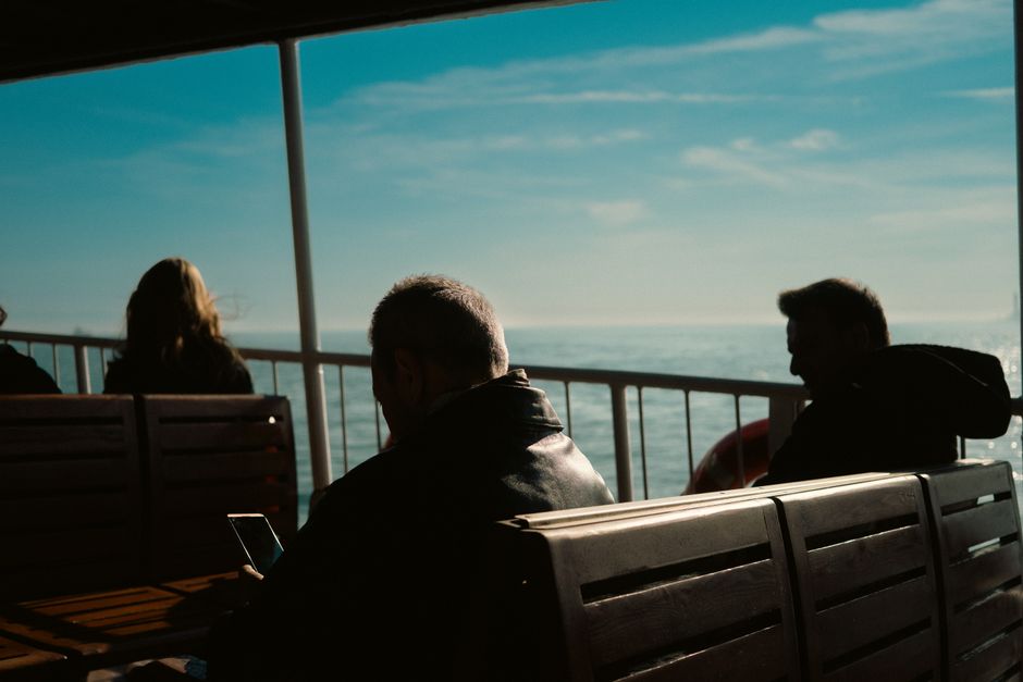 People enjoy a tranquil boat ride in sunlight, captured from behind passengers.
