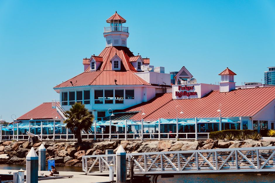 Scenic view of a lighthouse-themed restaurant on the seashore with clear blue skies.