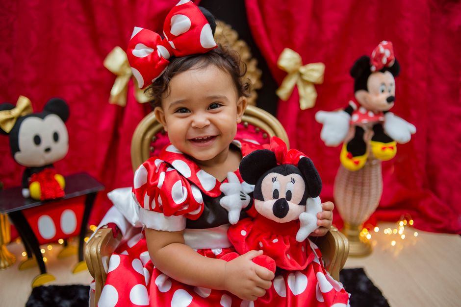 Charming toddler in a Minnie Mouse costume holding a plush toy and smiling brightly.