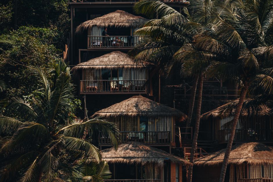 Relax in tropical wooden bungalows nestled among lush palm trees on a sunny beach.
