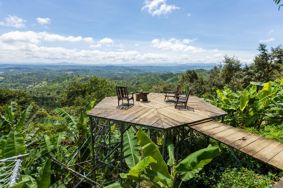 Scenic view from a wooden platform in a tropical forest with chairs facing the hills under a clear blue sky.