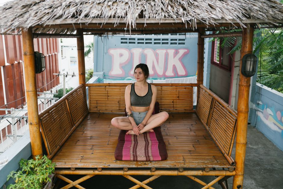 Full body of young female sitting in Lotus pose in traditional Asian gazebo during yoga session