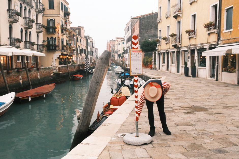 A gondolier stands beside a picturesque canal with charming Venetian architecture.