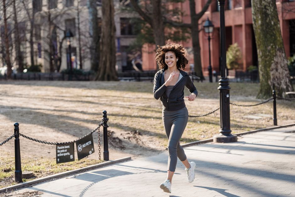 Full body of African American female jogger in sportswear smiling and running in park