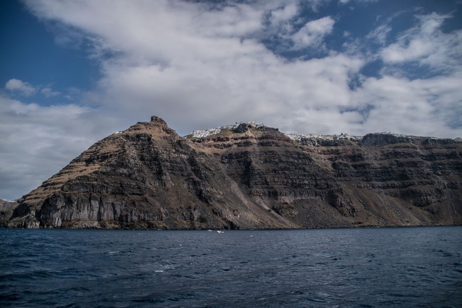 Breathtaking view of Santorini's rugged cliffs and azure sea under a partly cloudy sky.