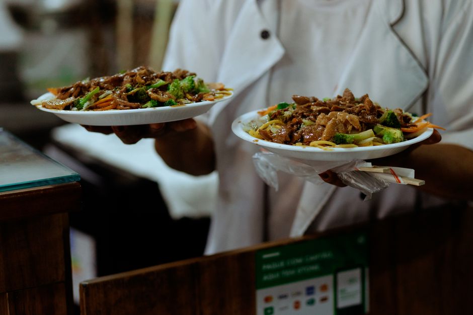 Close-up of a chef serving two plated Asian stir-fry dishes with beef and vegetables.