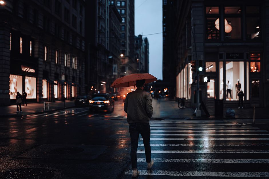 Man walking with red umbrella on rainy city street at night.
