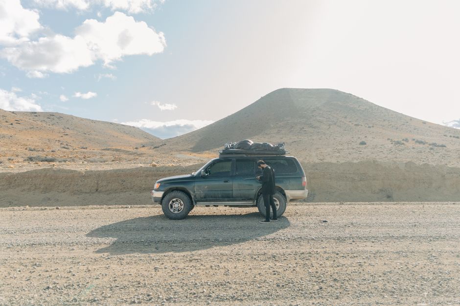 Man standing by SUV on a gravel road in Argentina's desert landscape, enjoying a road trip.
