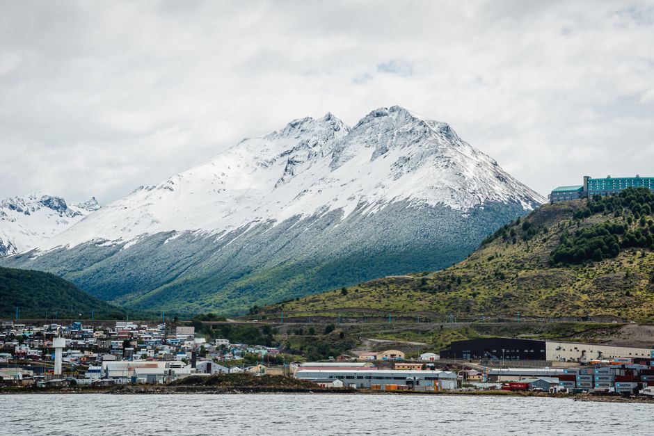 A picturesque view of snowcapped mountains and a coastal town under a cloudy sky.