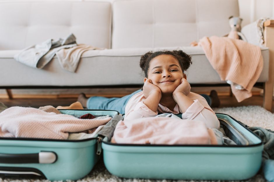 Smiling young girl lying in an open suitcase indoors preparing for travel.