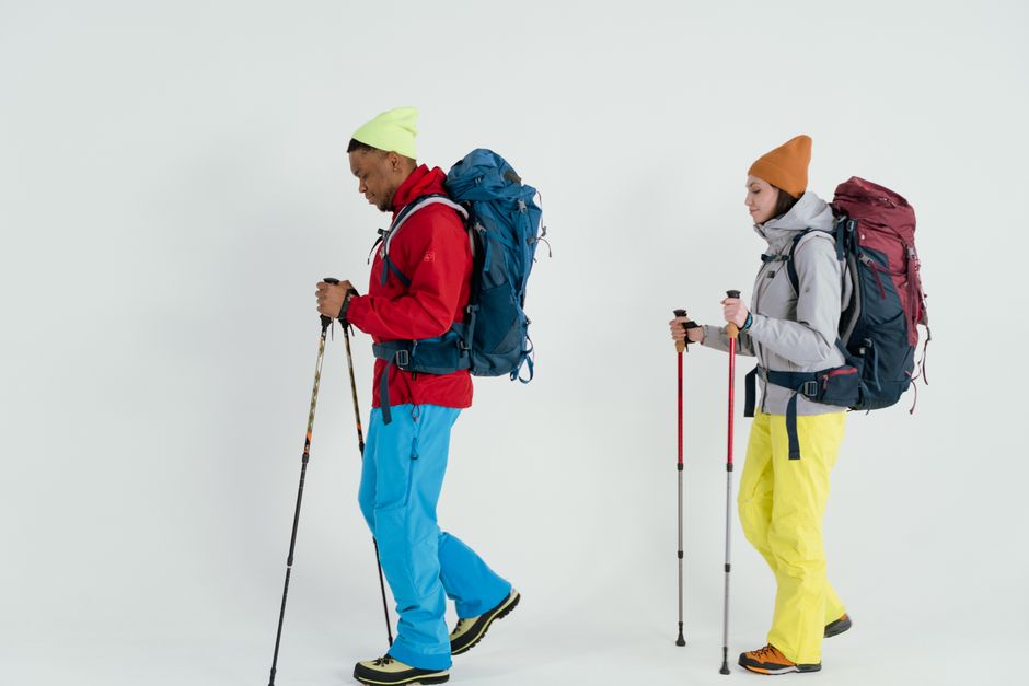Two hikers in vibrant winter gear with backpacks and ski poles on a white background.