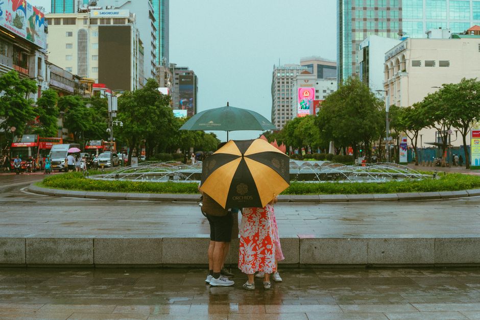 A rainy day in Ho Chi Minh City with a couple under umbrellas, showcasing vibrant city life.