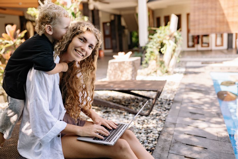 A joyful mother and child enjoying time together on a sunlit patio with a laptop.
