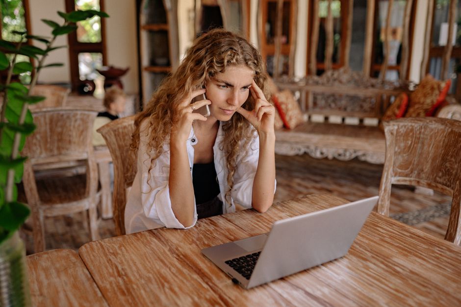 Focused woman multitasking with a phone and laptop in a cozy, rustic setting.