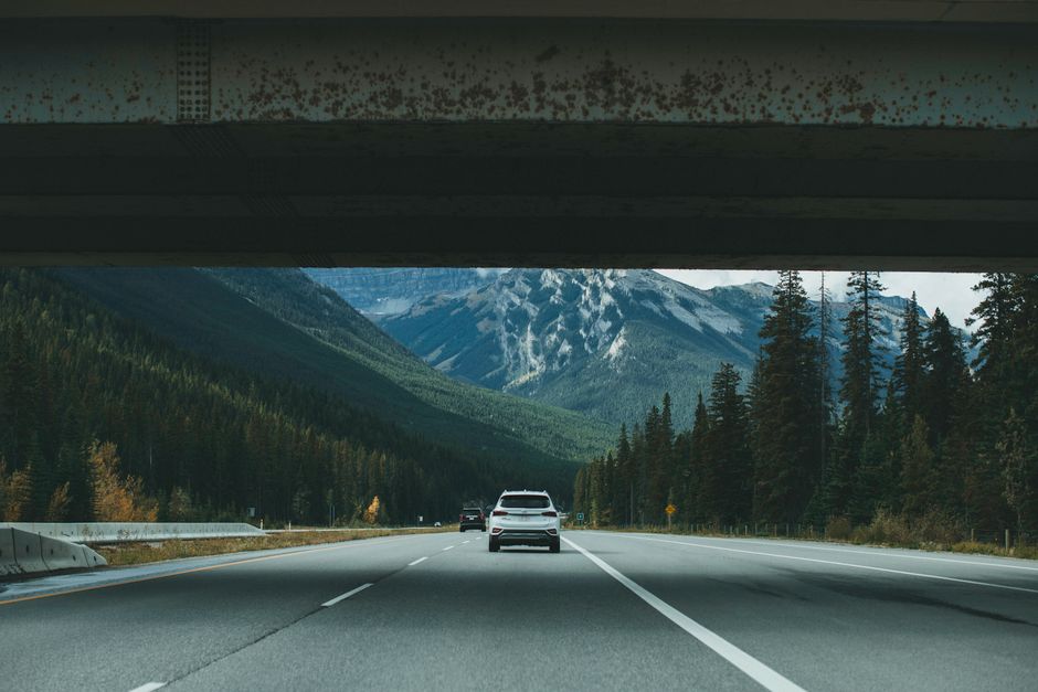 White car driving on a highway underpass with mountain views in the background.
