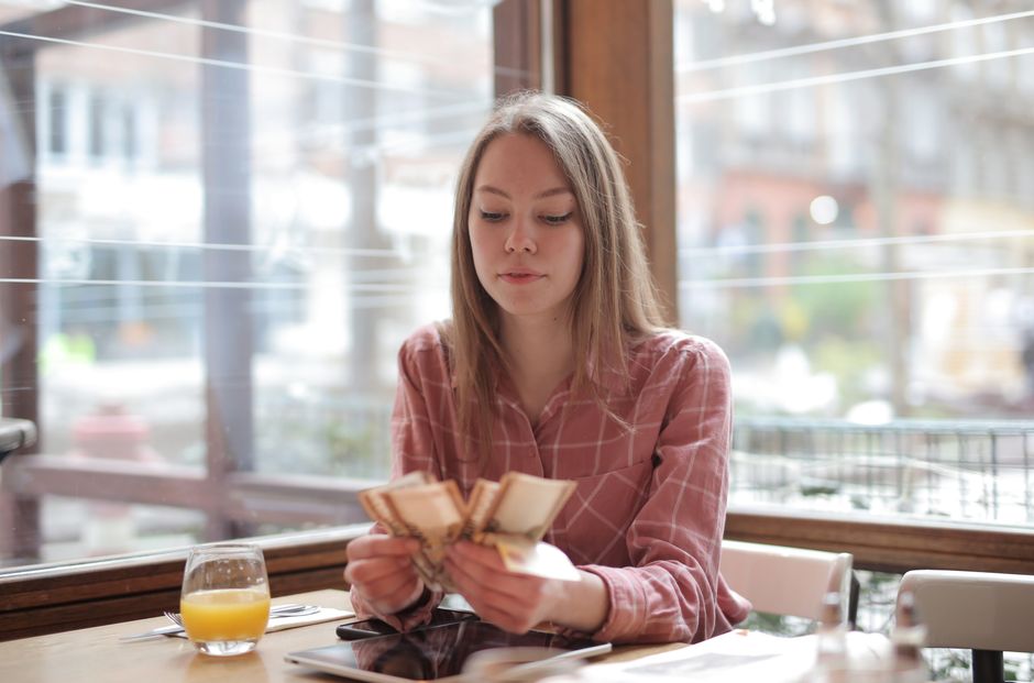 Young woman counting money in a cafe, showcasing modern lifestyle and leisure.