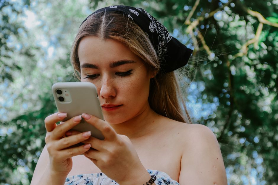Woman with a bandana focusing on her smartphone in a lush outdoor setting
