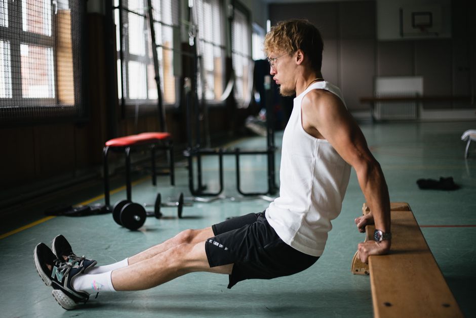 Side view of muscular sportsman in sportswear and glasses doing tricep dips exercises in g