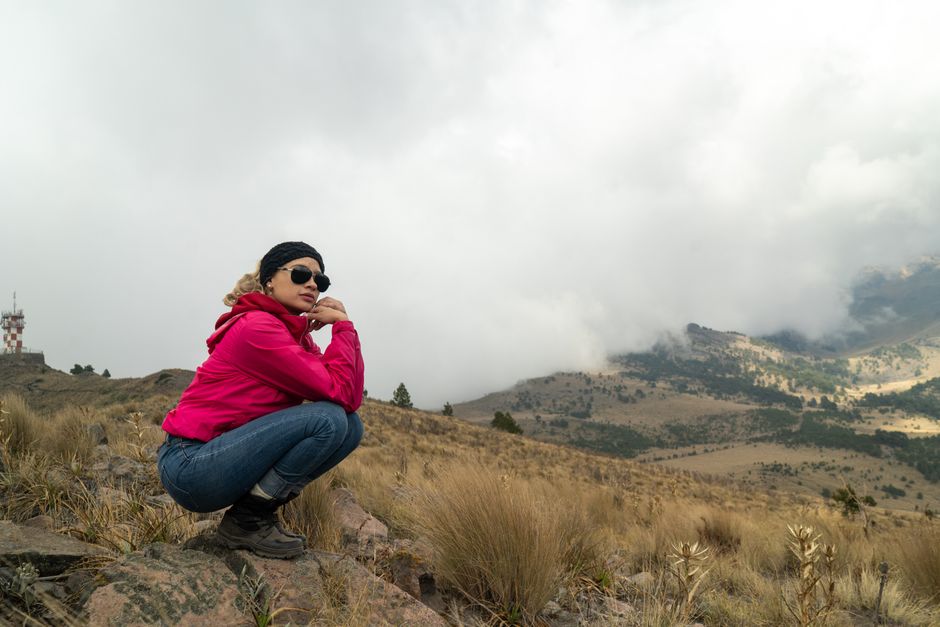 A woman in a red jacket enjoys a foggy mountain view, showcasing adventure and nature's beauty.