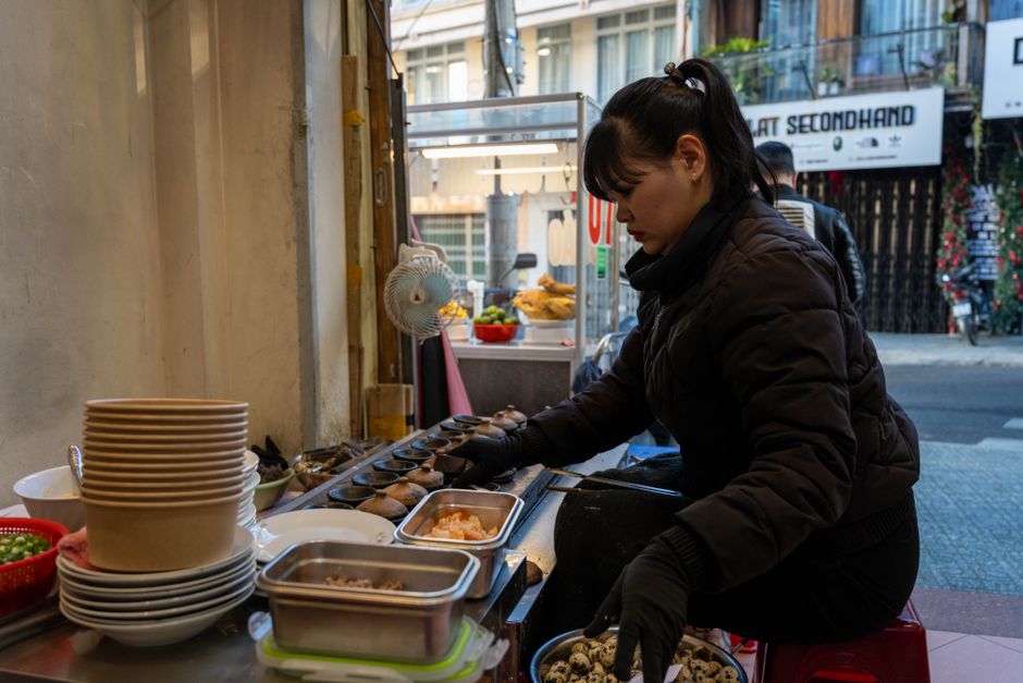 Female vendor prepares traditional street food outdoors in Dalat, Vietnam.