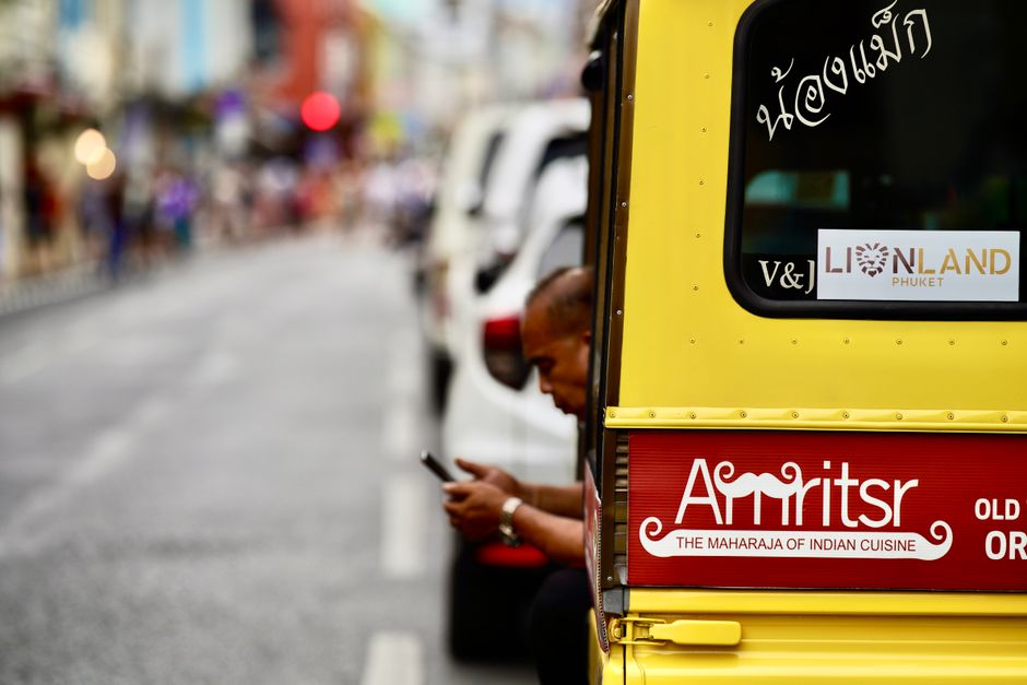 A vibrant street scene in Phuket featuring a tuk-tuk adorned with Indian restaurant signage.