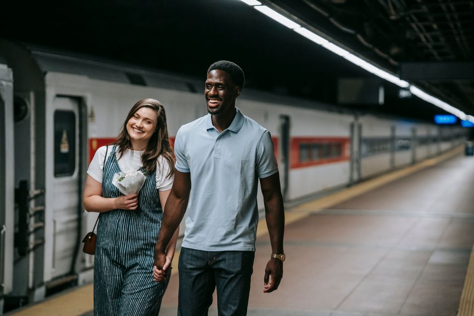Couple walking happily in a train station holding hands.