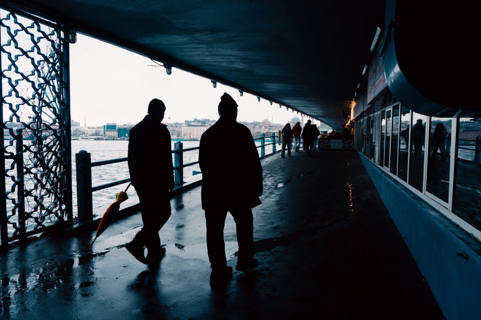 Silhouetted figures walking on Galata Bridge in Istanbul, capturing a moody, urban atmosphere.