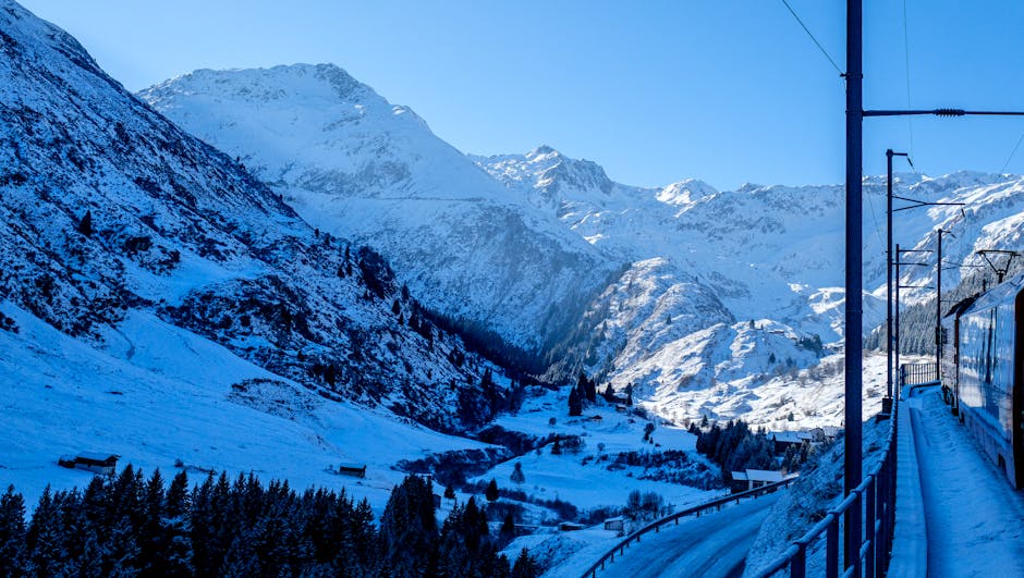 A picturesque winter train journey through snow-covered Swiss mountains captured on a clear day.
