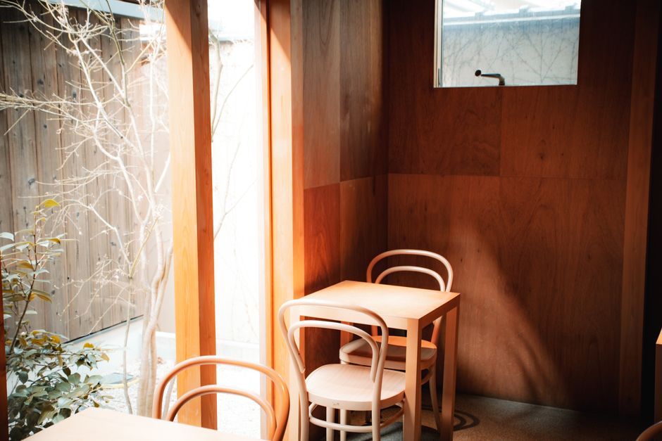 Bright and minimalist café interior with wooden tables and chairs illuminated by natural sunlight.