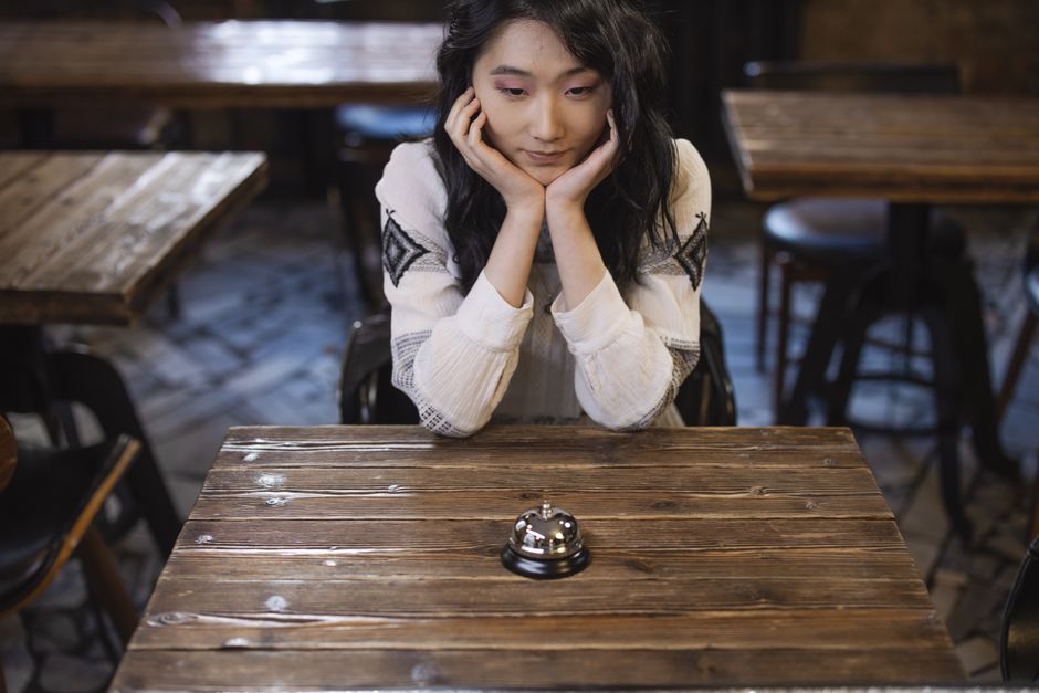 Young woman sitting at a wooden café table, lost in thought.